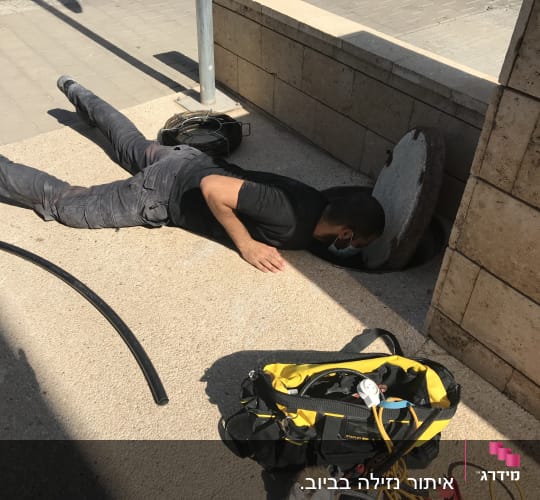 אדם בודק פתח ביוב עם תיק כלים צהוב